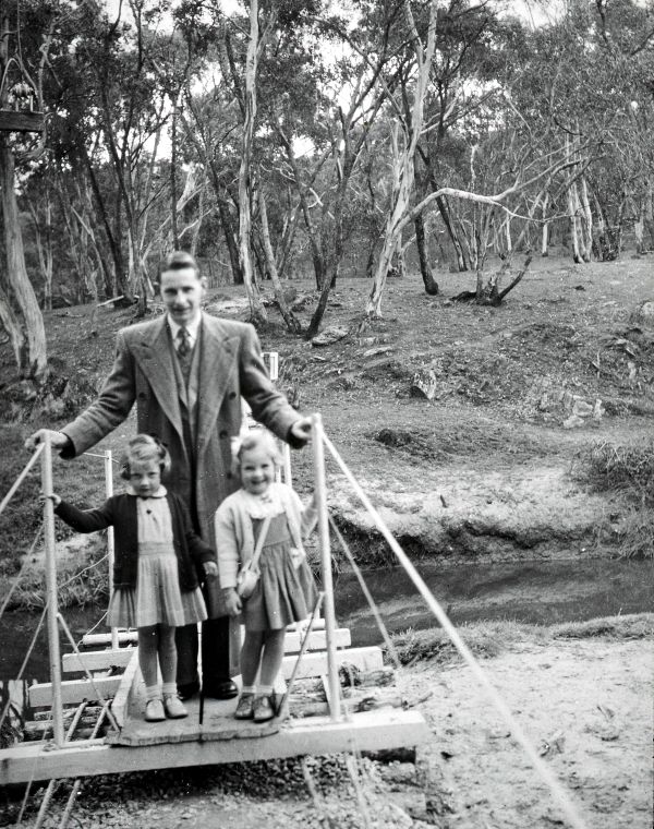 Dennis with two young girls on a footbridge.